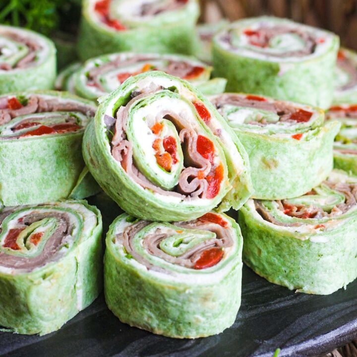 Close up of stack of roast beef pinwheels on a tray with parsley in background.