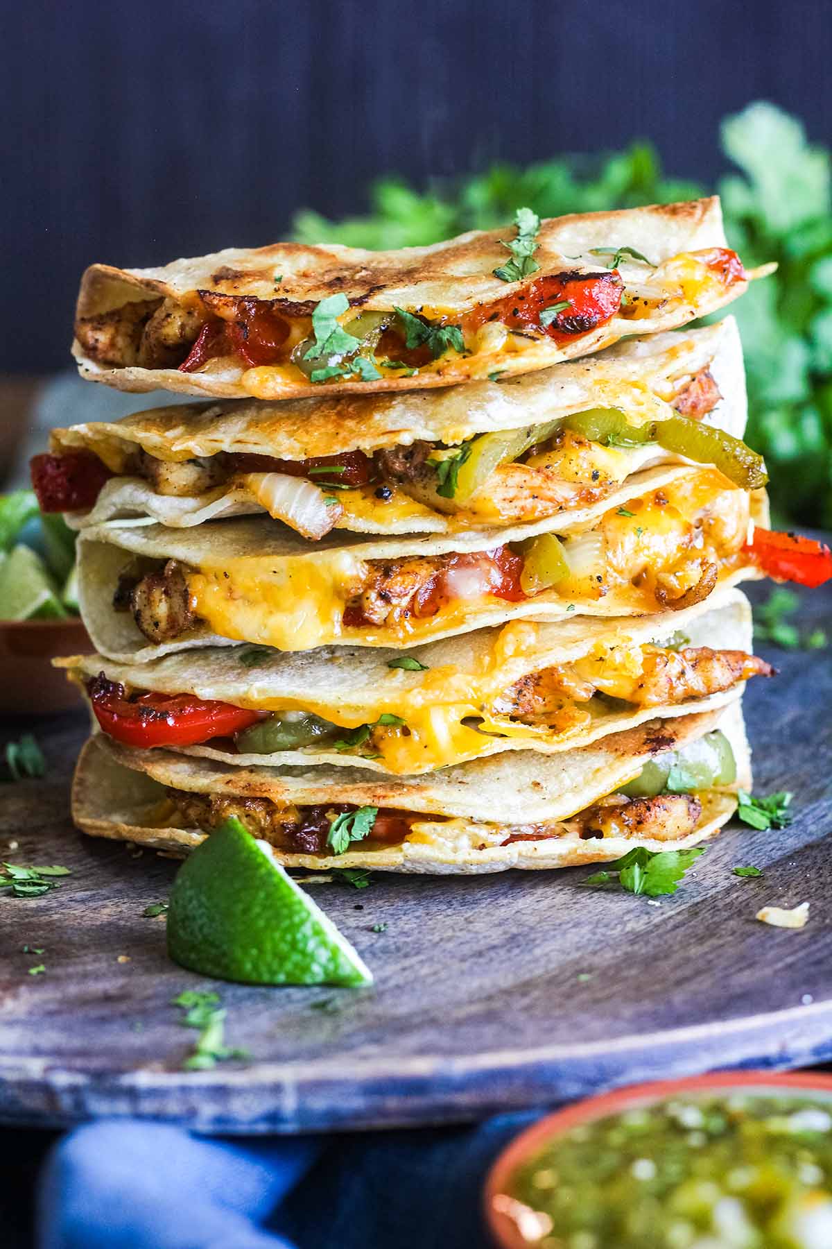 Stack of crispy chicken fajita tacos with a bowl of salsa and bunch of cilantro.