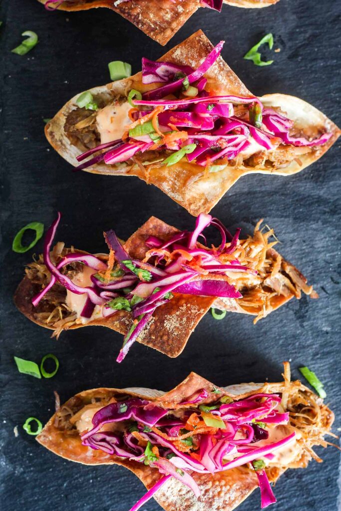 Three crispy wonton pork tacos wish scattered sliced scallitons.