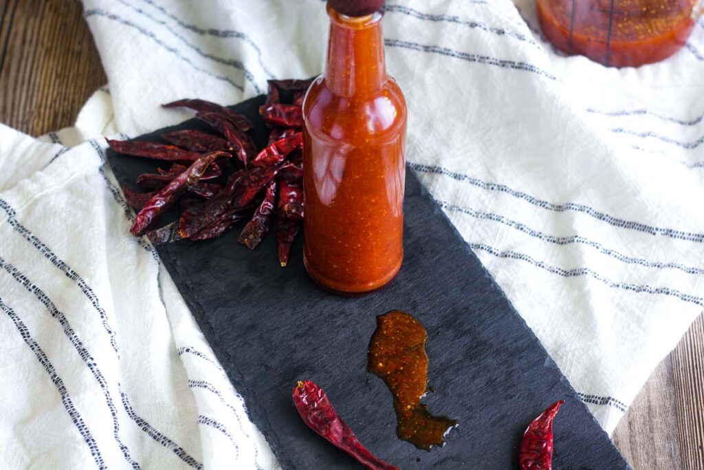 A slay tray with chiles and bottle of árbol sauce atop a kitchen towel.