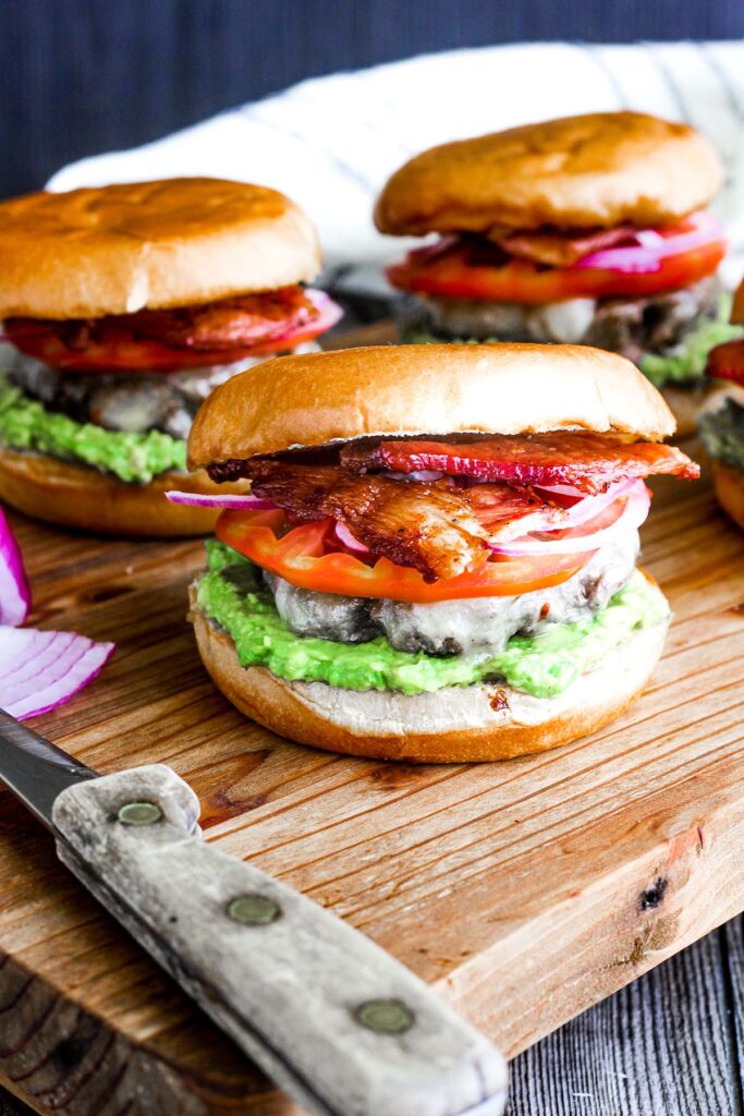 Bacon avocado burger aside a knife with more burgers in background.