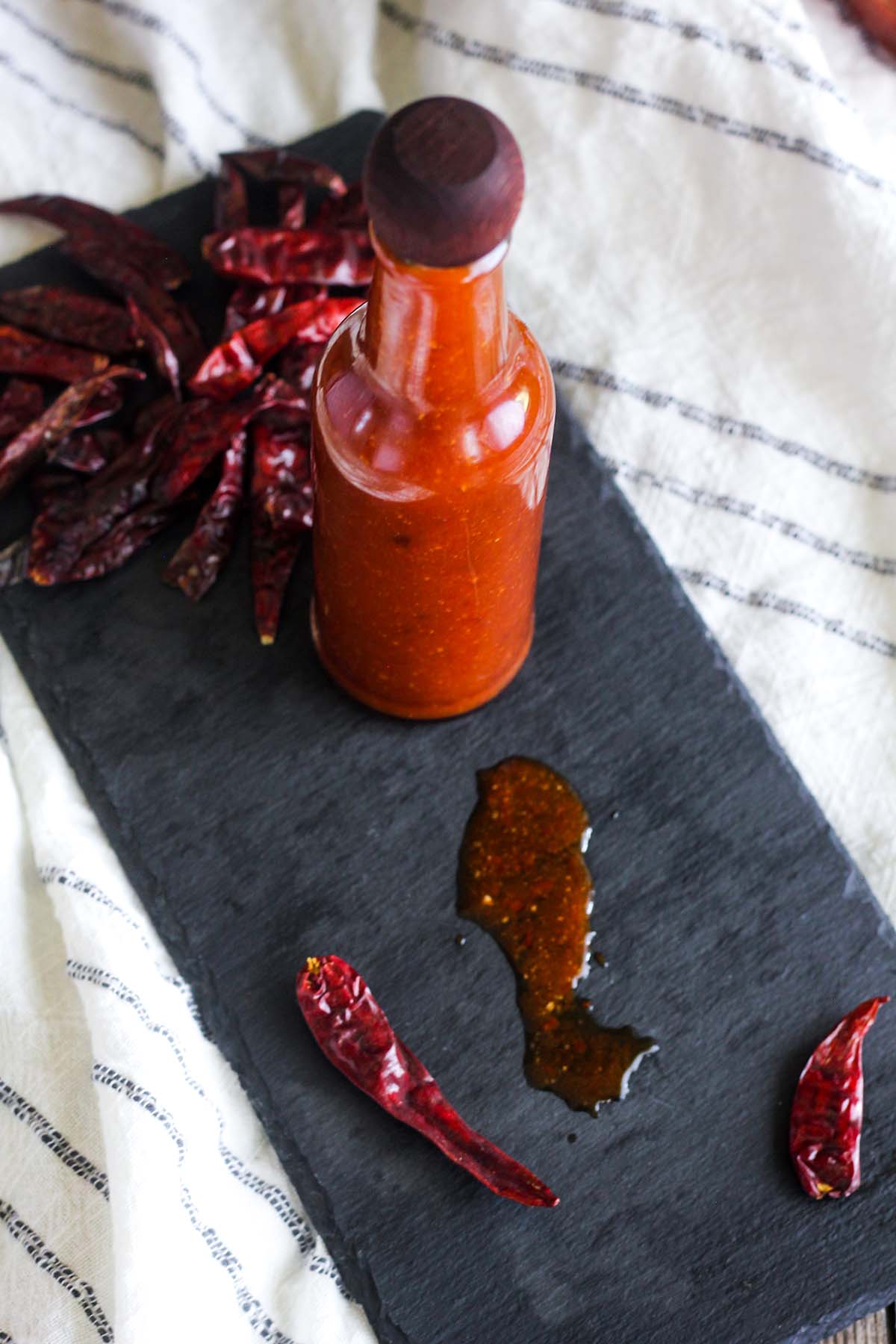 Bottle of hot sauce on a tray with scattered chiles.