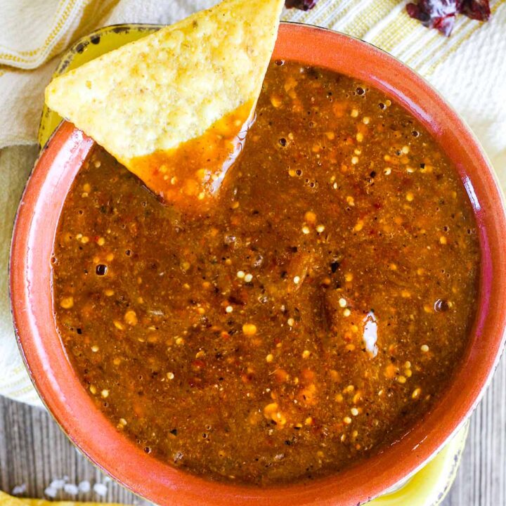 Bowl of salsa with a chip dipped in it surrounded by chiles and tortilla chips.
