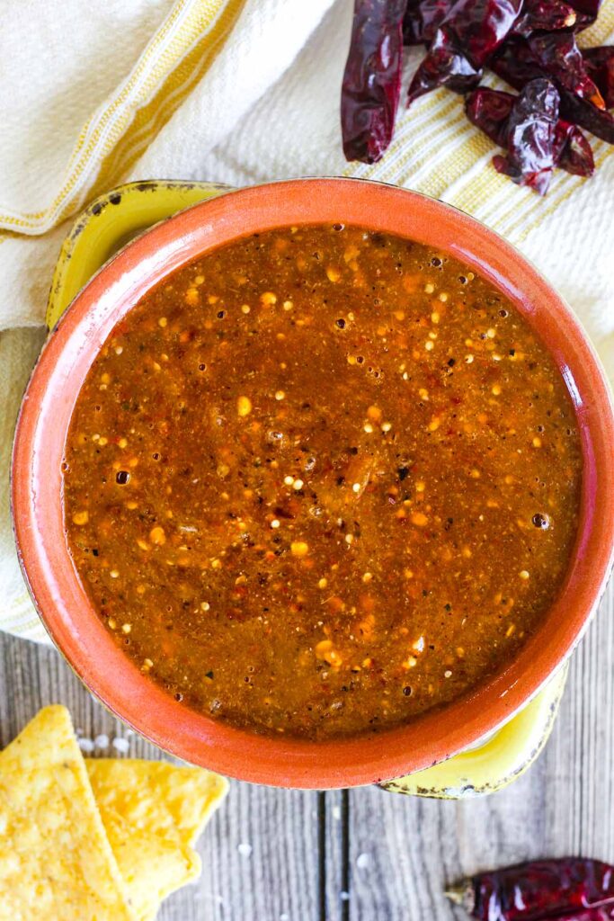 Chile de árbol salsa in a bowl surrounded by dried chiles and tortilla chips.