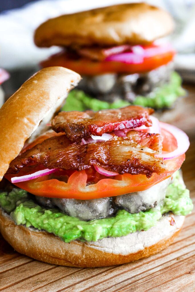 Close up of an avocado bacon burger with top bun leaning against it.