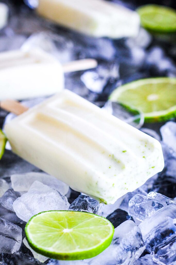 Close up of lime pop atop ice cubes with sliced limes.