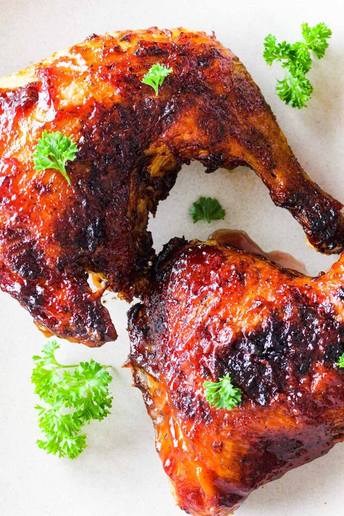 Close up of two pieces of barbecue chicken with sprigs of parsley.