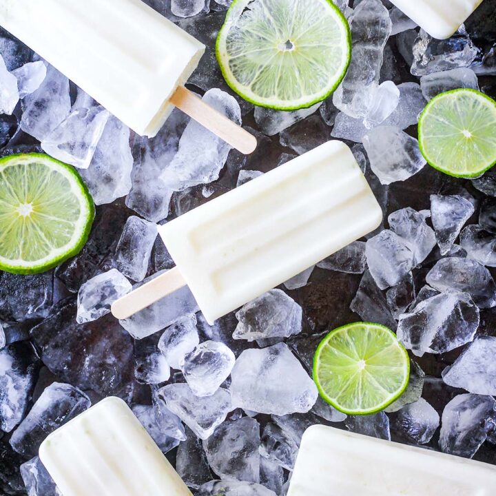 Creamy lime popsicles on a bed of ice cubes with sliced limes.