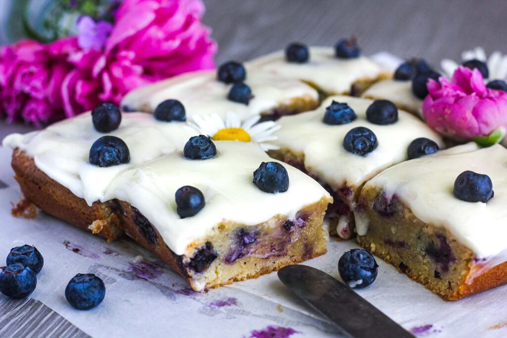 Frosted blueberry blondies topped with flowers and fresh blueberries.
