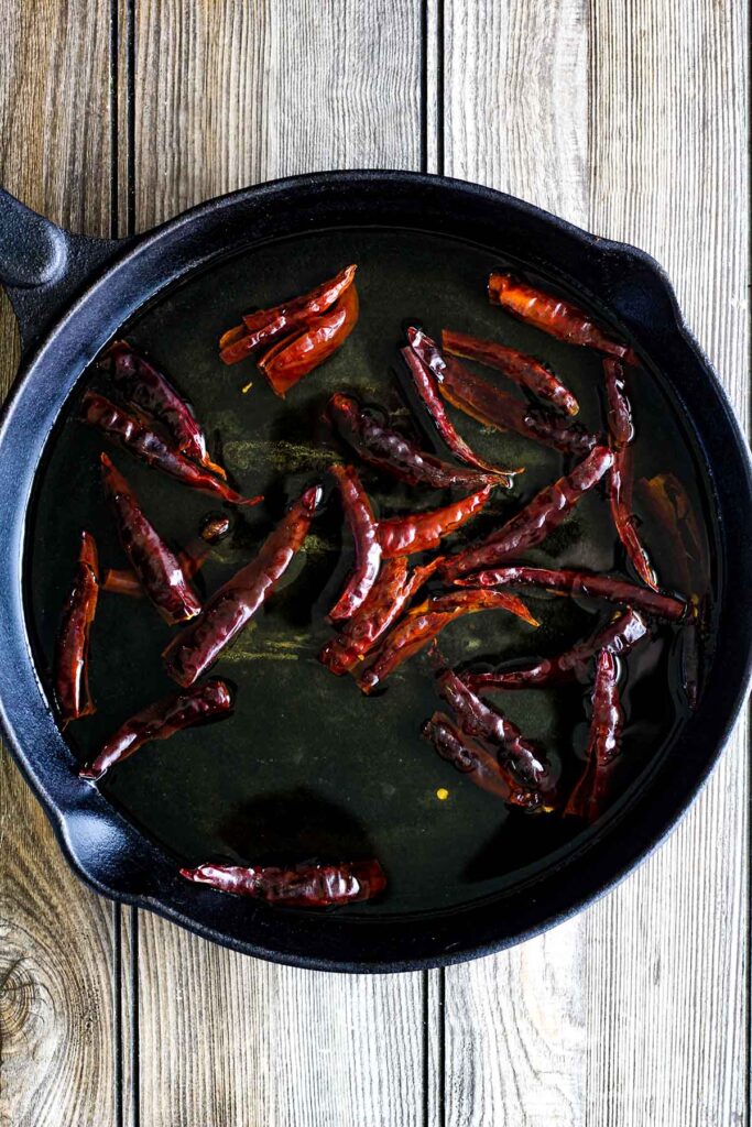 Toasted chiles submerged in water in a cast iron skillet.
