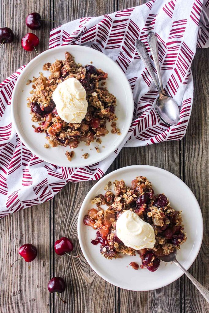Two plates of cherry apple crispy topped wiht a scope of ice cream with spoons.